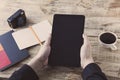 Digital tablet computer in male hands over cafe background - table wooden plancs, cup of coffee, nootbook, pencil, vintage camera. Royalty Free Stock Photo