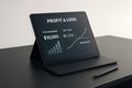 Digital tablet displaying profit and loss financial data with business chart graphics on a dark surface concept Royalty Free Stock Photo