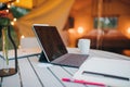 Digital tablet and notebook lying on table on background of Cozy open glamping tent with light inside during dusk. Luxury camping Royalty Free Stock Photo