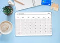 Digital tablet PC with calendar app show December\'2023 month screen and coffee cup, cactus, nootebook on blue workplace.