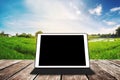 Digital tablet on wooden texture, at agricultural green field in sunrise, with black copy space on screen