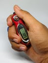 Digital tasbih counter held in hand, showing a close-up of a red and silver device with an LCD screen for counting.