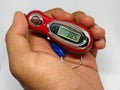Digital tasbih counter held in hand, showing a close-up of a red and silver device with an LCD screen for counting.