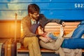 Digital technology and traveling. Young loving couple in hipster wear using tablet computer while sitting in the train station wai