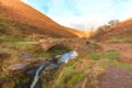 Digital watercolour of an autumnal waterfall and stone packhorse bridge at Three Shires Head in the Peak District.