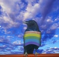 Digitally altered view of a rainbow striped black crow and blue sky with white clouds