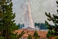 Digitally created watercolor painting of Old Faithful framed by pine trees, smoke filled sky and erupting in Yellowstone