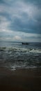 Dilapidated boat in choppy waters on a shoreline, illuminated by a menacing grey sky