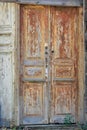 The dilapidated entrance door with the remains of brown paint with a handle and locks as a symbol of the abandoned life