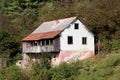 Dilapidated old family house with cracked facade and wooden balcony built on small hill surrounded with dense forest Royalty Free Stock Photo