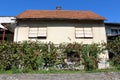 Dilapidated old suburban family house with closed window blinds and faded color facade surrounded with garden plants in front