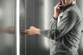 Diligent businessman pressing button inside elevator and talking on the phone. Man office worker in a grey shirt is pushing the