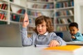 Schoolboy raising hand while using laptop in class