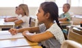 Diligent tween girl studying with classmates in elementary school