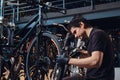 Diligent young mechanic is repairing customer`s bicycle at workplace