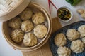 Dim sum aka dumplings,momos in a traditional bamboo steamer, with red chopsticks, Chinese cabbage & ginger root against white ba