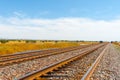 Diminishing perspective of raliway tracks through flat plains of New Mexico with distant mesa landforms under blue sky Royalty Free Stock Photo