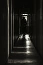 A dimly lit corridor with a solitary figure cloaked in shadows