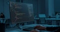 A dimly lit office space features a large computer monitor displaying lines of colorful Royalty Free Stock Photo