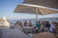 Diners eating outdoors on the banks of the River Tagus with the 25th of April bridge in background in Lisbon, Portugal
