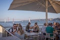 Diners eating outdoors on the banks of the River Tagus with the 25th of April bridge in background in Lisbon, Portugal