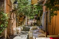 Diners sitting in outdoor cafes in narrow alley under dappled sunlight in Crete, Greece