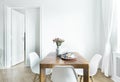 Dining table with fresh flowers and breakfast tray with coffee cup and fruits in real photo of white room interior with empty wall Royalty Free Stock Photo