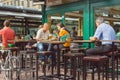 Dinner of busy people in outdoor city cafe with tall wooden tables and chairs