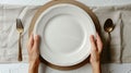 The dinner place setting has an empty white plate with a hand holding a silver fork and spoon on a white background. The Royalty Free Stock Photo