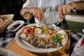 Dinner at the restaurant. Mediterranean food. Grilled fish and vegetables on a plate. Hands of a man cutting fish in a plate Royalty Free Stock Photo