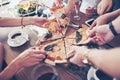 Dinner time. Close-up of tasty pizza on the table, with a lot of hands that take a piece