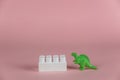 A dinosaur miniature and a white block of children`s constructor against a pink background. Small green miniature of a predatory