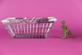 A dinosaur and a shopping cart against a purple background. Shiny empty shopping cart. Green miniature of a predatory animal