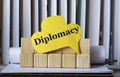 DIPLOMACY - word on yellow paper against the background of wooden cubes and standing books