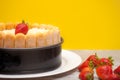 Diplomat cake or Charlotte Cake with strwaberries and lady fingers in baking pan on a wooden table with yellow background / Focus Royalty Free Stock Photo