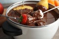 Dipping fresh fruits into pot with tasty chocolate fondue,