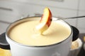 Dipping fresh peach into pot with chocolate fondue