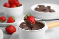 Dipping strawberry into fondue pot with chocolate on table, closeup