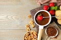 Dipping strawberry into fondue pot with milk chocolate on wooden table, flat lay