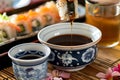 dipping sushi into soy sauce bowl with sake cup beside Royalty Free Stock Photo