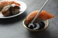 Dipping tasty nigiri sushi with salmon into soy sauce on grey table, closeup Royalty Free Stock Photo