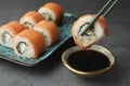 Dipping tasty sushi roll with salmon into soy sauce on grey table, closeup Royalty Free Stock Photo