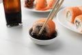 Dipping tasty sushi roll with salmon into soy sauce on white table, closeup Royalty Free Stock Photo