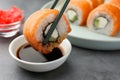 Dipping tasty sushi into soy sauce at grey table, closeup Royalty Free Stock Photo