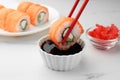 Dipping tasty sushi into soy sauce at white marble table, closeup Royalty Free Stock Photo