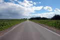 Direct empty suburban road through the field and forest with stormy clouds on one side of the sky