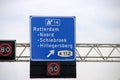 Direction sign in blue and white heading Rotterdam Noord, Schiebroek and Hilligersber S112 on motorway A20 with speed limits