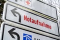 Direction sign shows the Red Cross and German text Notaufnahme, meaning emergency department, at the driveway to a large hospital