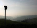 Direction sign in silhouette over misty landscape at daybreak with mist covered hills and valley just before sunrise