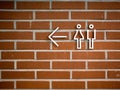 A directional sign to the toilet in a background of red bricks. A white finger post with symbols of male and female. Royalty Free Stock Photo